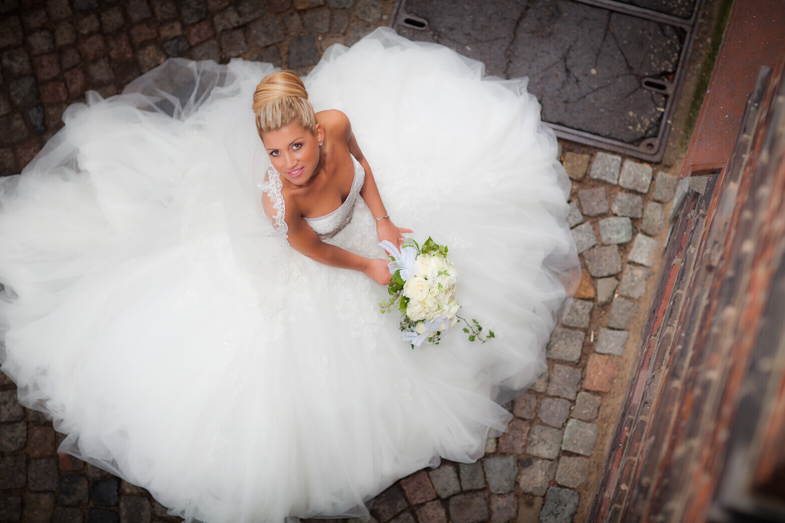Braut mit Brautstrauß blickt aus dem ausgebreiteten Tüllkleid nach oben