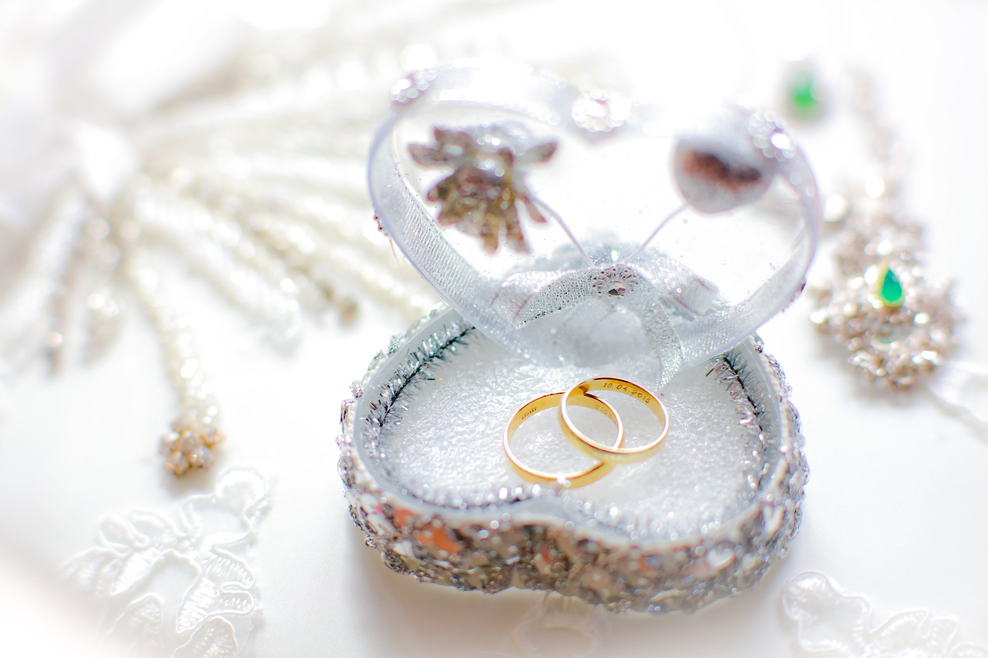 Zwei goldene Eheringe liegen in einer offenen herzförmigen Schatulle mit Schmuck im Hintergrund, Hochzeitsfotograf Hamburg